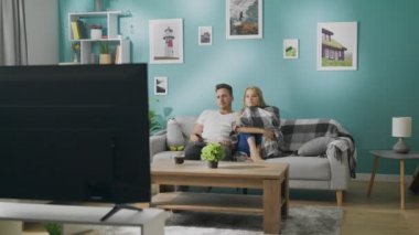Canı sıkılan genç çift kanepede televizyon izliyor