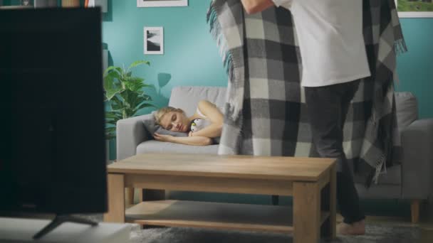Mladý muž kryje spící přítelkyni s přikrývkou na gauči v obývacím pokoji — Stock video