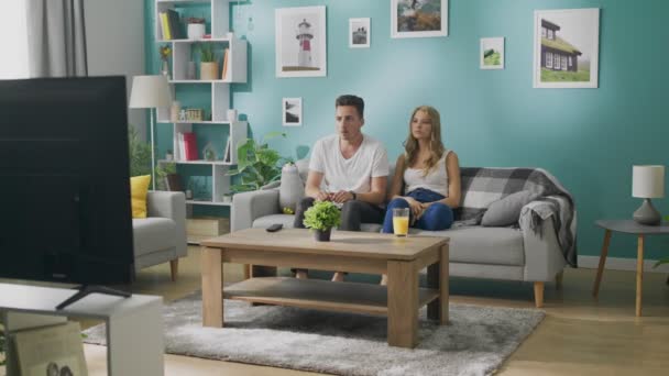 Young couple watching a scary movie on TV on the couch in a cozy living room — Stock Video