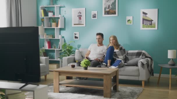 Скучная молодая пара смотрит телевизор на диване — стоковое видео