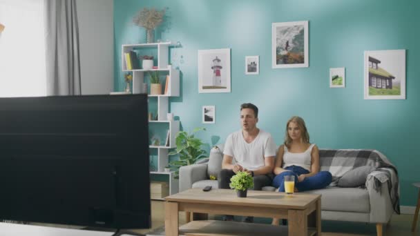 Pareja joven viendo deportes en la televisión en un sofá en una acogedora sala de estar — Vídeo de stock