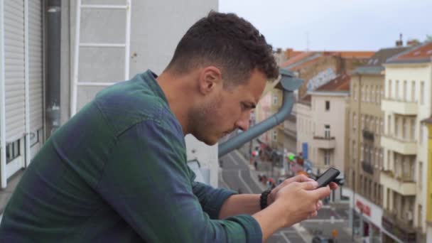 Homem digitando sms em uma varanda no hotel em uma cidade grande — Vídeo de Stock