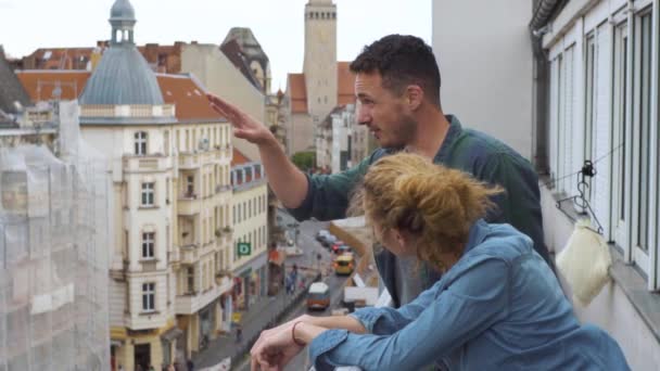Νεαρό ζευγάρι στο μπαλκόνι ενός ξενοδοχείου στο κέντρο μιας μεγάλης πόλης σε ένα ταξίδι — Αρχείο Βίντεο