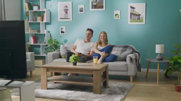 Feliz jovem casal assistindo tv no sofá na acolhedora sala de estar — Vídeo de Stock