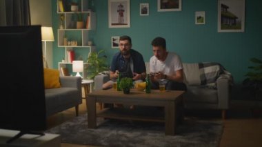 Oturma odasında bir kanepede akşam Iki arkadaş ve video oyunları oynarken