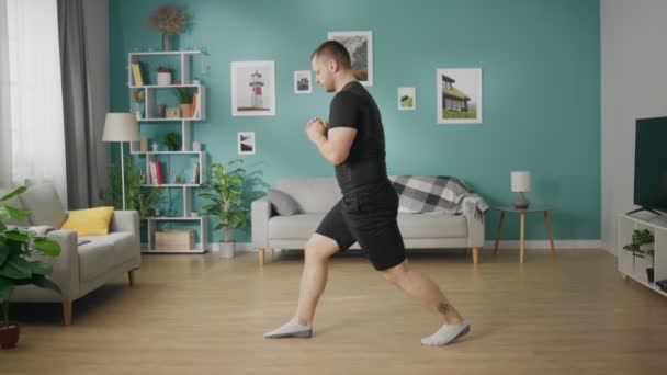 Un joven hace deporte durante el día en su sala de estar — Vídeo de stock