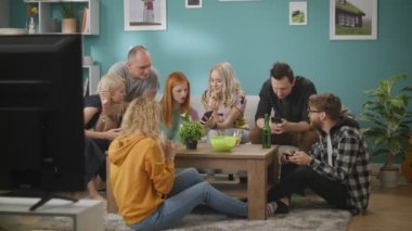 Genç arkadaşlar kanepede oturan ve ev partisi sırasında her zaman telefonlarını kullanarak