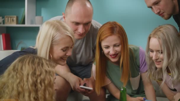 Группа счастливых друзей смотрят смешные мемы на смартфоне, сидя на диване — стоковое видео