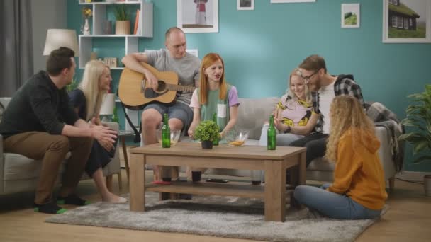 Grupo de amigos cantam músicas enquanto seu amigo toca guitarra na sala de estar — Vídeo de Stock