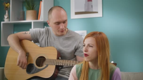 Група друзів співають пісні, а їх друг грає на гітарі у вітальні — стокове відео
