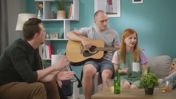 Grupo de amigos cantam músicas enquanto seu amigo toca guitarra na sala de estar — Vídeo de Stock