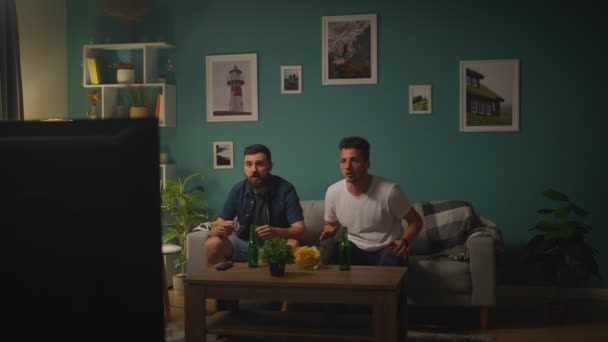 Twee vrienden kijken voetbalwedstrijd op TV thuis, juichen beste voetbalteam — Stockvideo