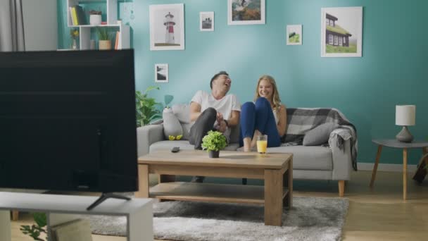 Feliz joven pareja viendo la televisión en el sofá en acogedora sala de estar — Vídeos de Stock