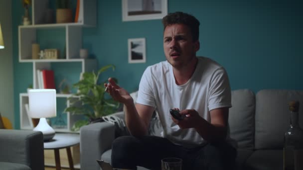 Мужчина пьет пиво или коктейль из стекла и смотрит телевизор дома — стоковое видео