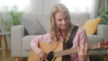 Güzel kadın onun oturma odasında gitar oynuyor