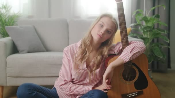 Ένας νεαρός άντρας φωτογραφίζει ένα κορίτσι με μια κιθάρα στο σπίτι της. — Αρχείο Βίντεο