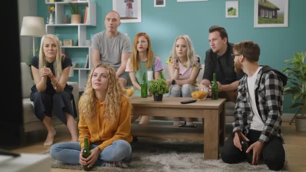 En la sala de estar Grupo de amigos en ver la televisión, y bebe cerveza con bocadillos — Vídeos de Stock