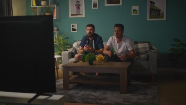 Zwei Freunde vor dem Fernseher schauen sich auf der Couch ein Spiel Sport an — Stockvideo