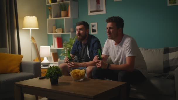 Dva mladí muži spolu mluví a začínají se rozčilovat při sledování sportovní hry v televizi — Stock video