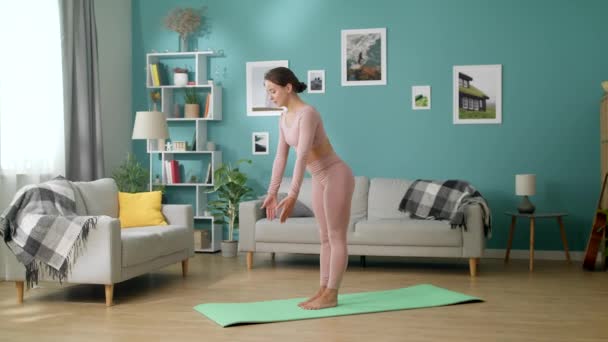 Junge Frau im Wohnzimmer praktiziert Yoga, balanciert auf einem Bein — Stockvideo