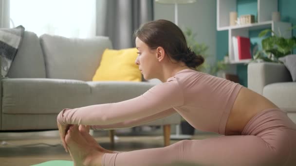 Jonge atletische vrouw in roze Sportswear doen yoga en stretching in de woonkamer — Stockvideo