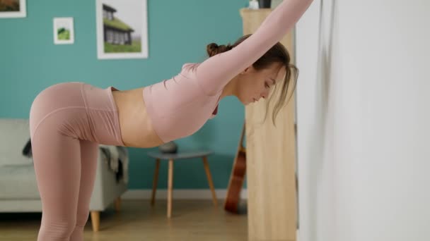 Mulher esticando e dobrando-se contra a parede em casa — Vídeo de Stock