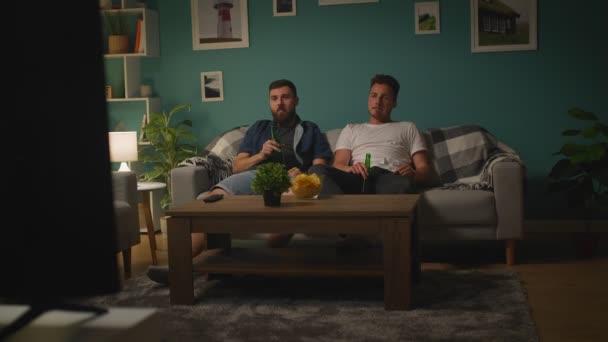 Zwei junge Männer unterhalten sich und regen sich auf, während sie zu Hause ein Sportspiel im Fernsehen verfolgen — Stockvideo