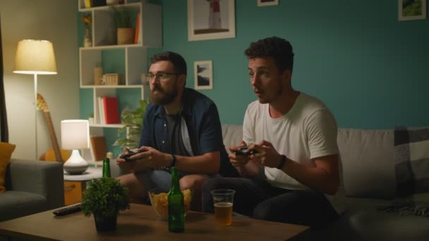 Im Wohnzimmer sitzen zwei Freunde auf einer Couch und spielen wettbewerbsfähiges Videospiel — Stockvideo