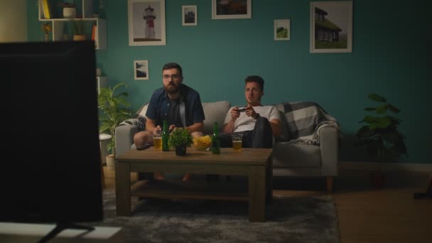 Im Wohnzimmer sitzen zwei Brüder auf einer Couch und spielen Videospiele — Stockvideo