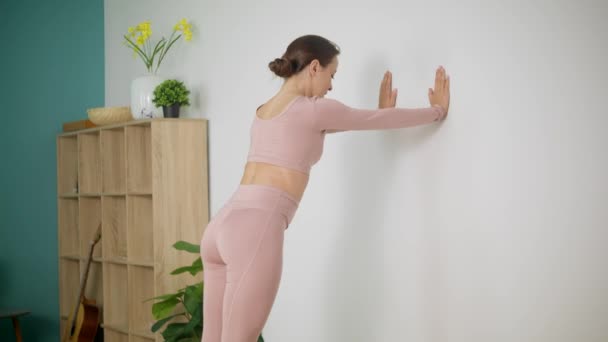 Nő csinál stretching a fal közelében a nappaliban — Stock videók