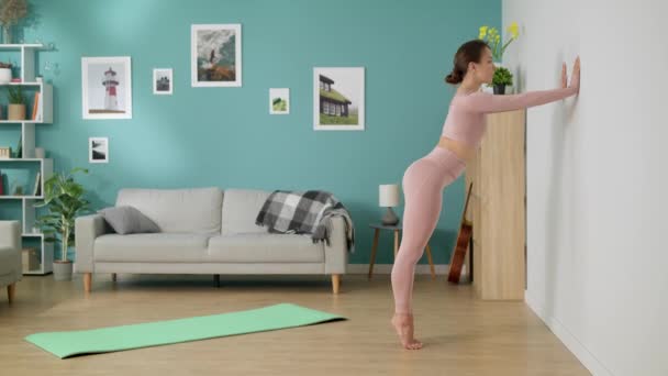 Mulher esticando e dobrando-se contra a parede na sala de estar — Vídeo de Stock