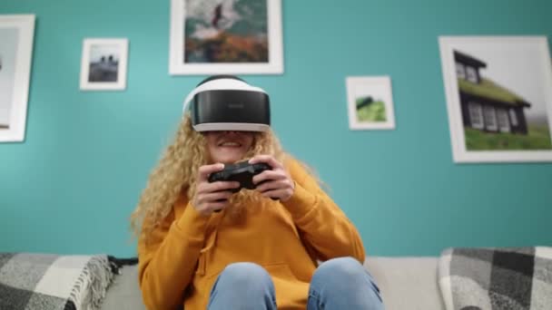 Mulher de capuz amarelo e óculos VR joga jogos de ação com gamepad — Vídeo de Stock