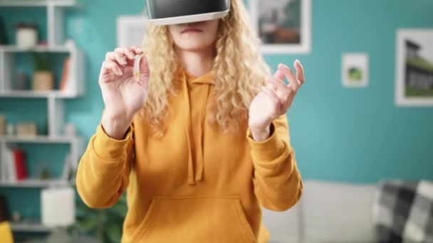 Mulher com capuz amarelo óculos VR acenando as mãos na acolhedora sala de estar — Vídeo de Stock