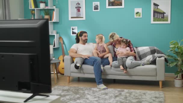 Mamá papá y los niños pequeños ven la televisión en casa sentado en el sofá — Vídeos de Stock