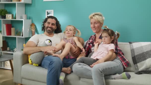 Счастливая семья мама папа и дочери смотреть смешные мультики сидеть на диване дома — стоковое видео