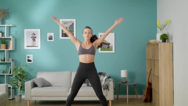 Bella donna magra fa esercizi cardio mattutini saltando jack in camera moderna — Video Stock