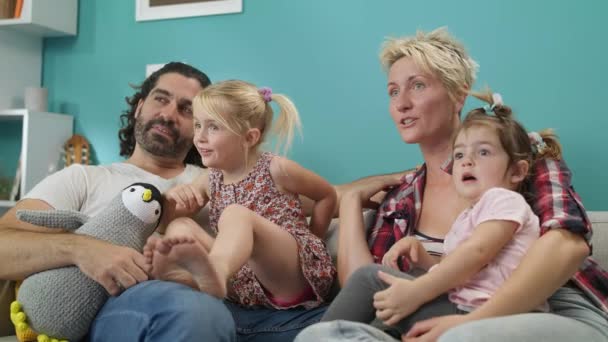 Lycklig familj mamma pappa och döttrar titta på rolig TV-show sitta på soffan hemma — Stockvideo