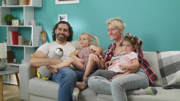 Familia feliz viendo la televisión. Pareja con niños se sienta en un sofá gris y se ríe . — Vídeos de Stock