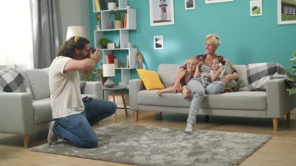 Man fotografeert zijn vrouw en dochters op een professionele camera in de woonkamer — Stockvideo