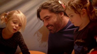 Baba, akşamları oyuncak çadırında kızlarına kitap okur.