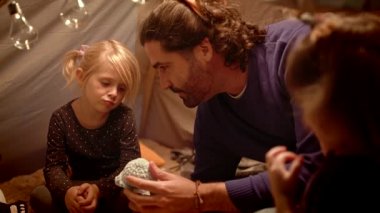 Kızları olan baba evde bir çadırda oyuncak balina ile oynuyor.