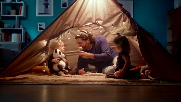 Dad with daughters in a tent at home. Dad imitates a penguin. — Stock Video