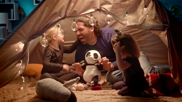 Pappa med döttrar leker med en leksaks Panda i ett tält hemma. — Stockvideo