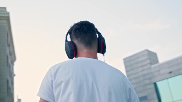 Homem caminha pela cidade e ouve música em fones de ouvido — Vídeo de Stock