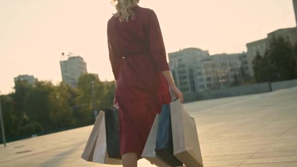 Mujer con bolsas de compras caminando en una ciudad al atardecer. Movimiento lento — Vídeo de stock