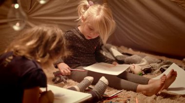 İki küçük kız kardeş geceleri odada dekoratif bir çadırda kalemle çizin