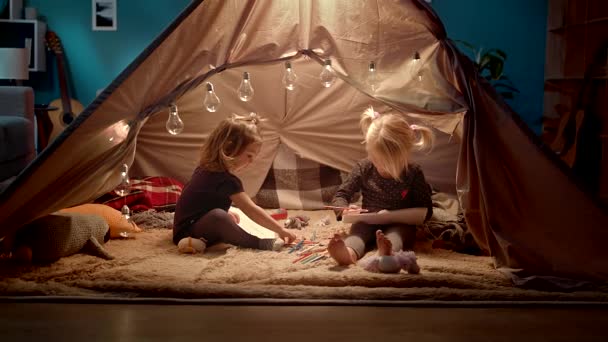 İki küçük kız kardeş odada dekoratif bir çadırda kalemile çizmek. — Stok video