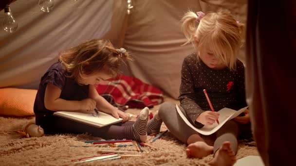Małe siostry rysują ołówków w ozdobnym namiocie w pokoju. — Wideo stockowe