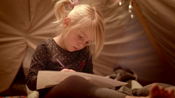 Portret małej dziewczynki czerpie z dekoracyjnego namiotu w pokoju nocą — Wideo stockowe
