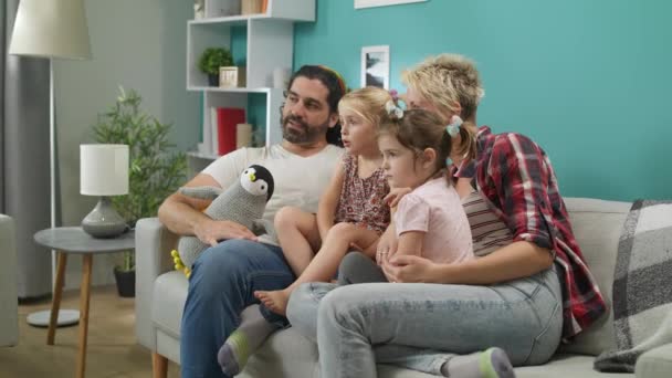 Feliz familia ver dibujos animados en casa sentado en el sofá — Vídeo de stock